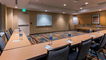 A conference room with a long table, chairs, water bottles, name cards, a projector screen, and a whiteboard.