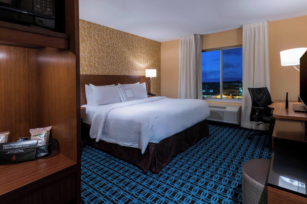 A hotel room with a large bed, a desk with a chair, a TV, and a window with curtains.