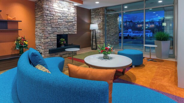 A modern lobby with a stone fireplace, blue seating, and a view of parked cars outside. - Fairfield Inn & Suites Boston Marlborough/Apex Center (Marlborough)