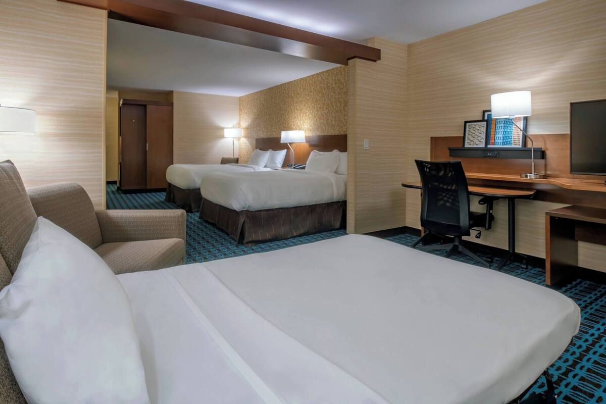 A hotel room with two beds, a desk, a chair, and a TV.