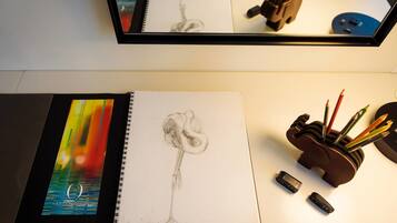 A sketchbook with a drawing, a notebook with a colorful cover, and a pencil holder with pencils and a USB drive.