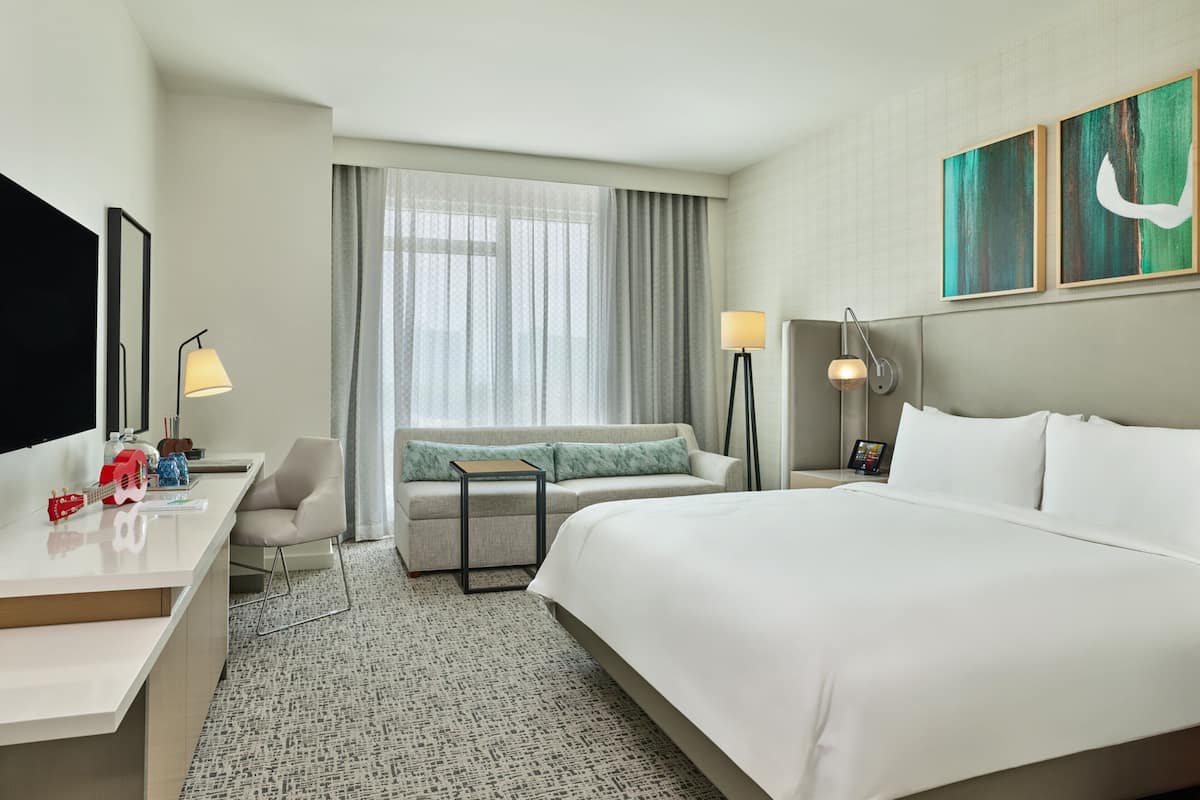 Een hotelkamer met een groot bed, een bureau, een stoel, een kleine tafel en een raam met gordijnen.