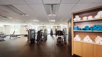A gym with exercise equipment, wooden cabinets with towels, and large windows.