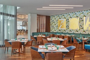 A modern dining area with multiple tables and chairs, a patterned wall, and a seating area with blue upholstered benches. - Art Ovation Hotel, Autograph Collection (Sarasota)
