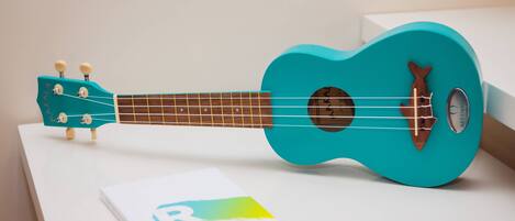 Un ukelele turquesa sobre una superficie blanca, con un libro titulado 'Exploring the Caribbean Islands' a su lado.