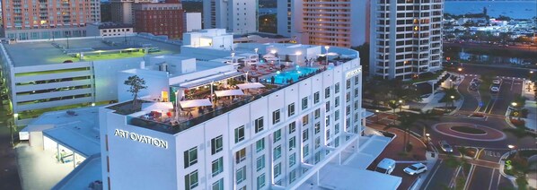 A hotel with a rooftop pool area, outdoor seating, and a view of the surrounding cityscape.