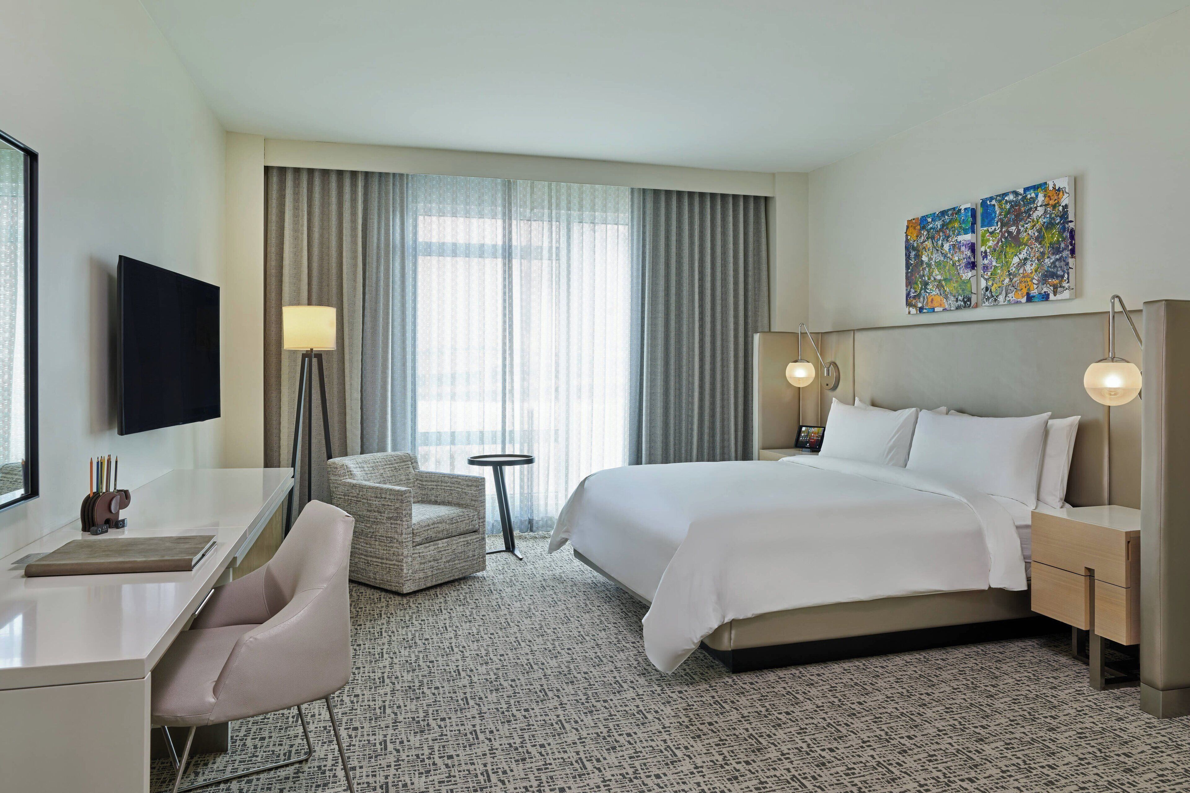 Une chambre d’hôtel avec un grand lit, un bureau avec une chaise, une télévision et une lampe.