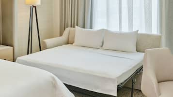 A hotel room with a bed, a chair, a floor lamp, and a window with curtains.
