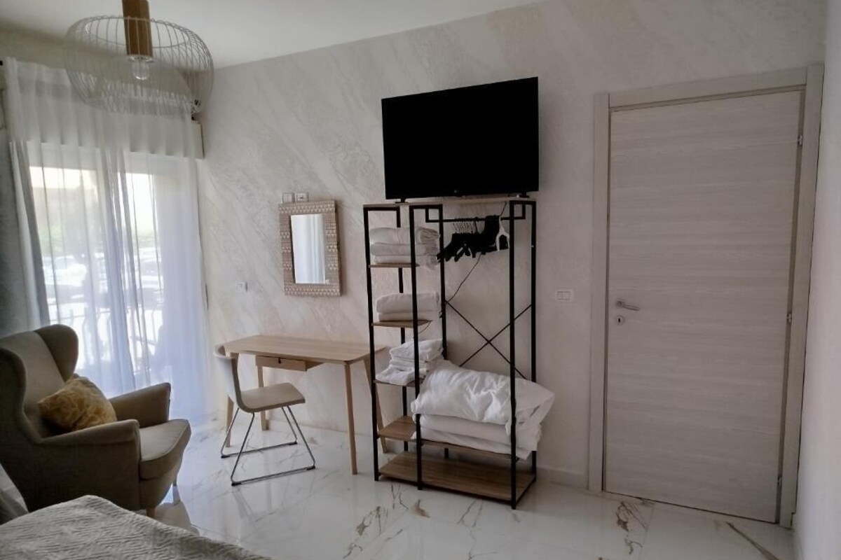 Quarto de hotel com cama, escrivaninha, cadeira, televisão presa à parede e guarda-roupa.