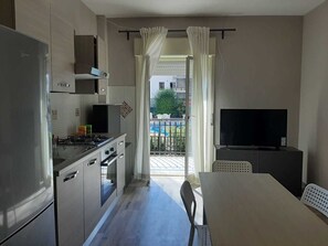 Cozinha compacta com eletrodomésticos modernos, espaço de jantar e varanda com vista para a piscina.