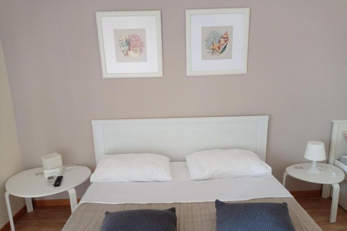 Quarto de hotel com uma cama, duas mesas de cabeceira e duas obras de arte emolduradas na parede.