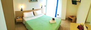 A hotel room with a bed, bedside table, lamp, and a small table with a flower arrangement. - Hotel Atlantic (Senigallia)
