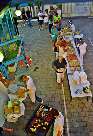 An outdoor buffet setup with multiple food stations and attendees. - Hotel Atlantic (Senigallia)