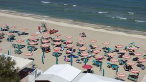 A beach with rows of sunbeds and umbrellas, a lifeguard tower, and the ocean in the background.
