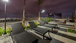 Eine Dachterrasse mit Liegestühlen und Geländer mit Blick auf eine beleuchtete Stadtlandschaft.