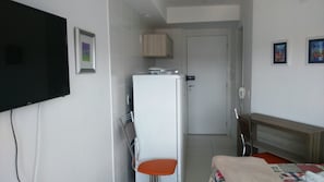 Habitación de hotel con cama, televisión, refrigerador, silla y mesita de noche.