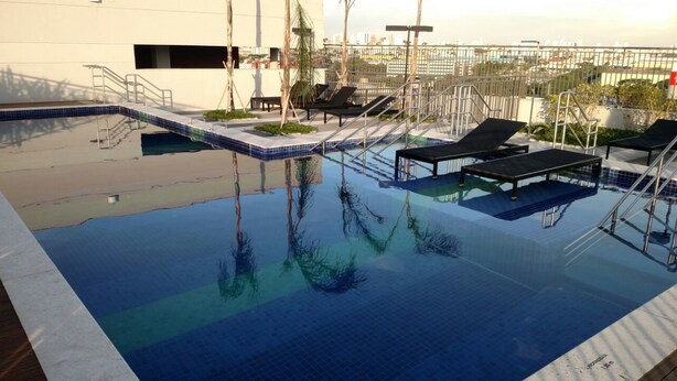 Ein Pool auf dem Dach mit klarem, blauem Wasser, Liegestühlen und Blick auf die Stadtlandschaft.