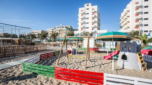 Un parque infantil en la playa con columpios, toboganes y una estructura con forma de castillo de arena.