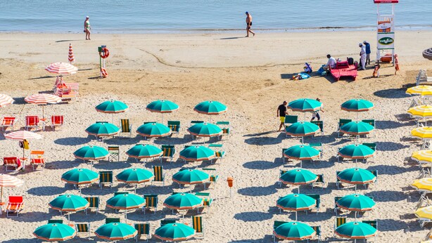 Una playa con hileras de sombrillas azules y verdes y sillas de playa a rayas.