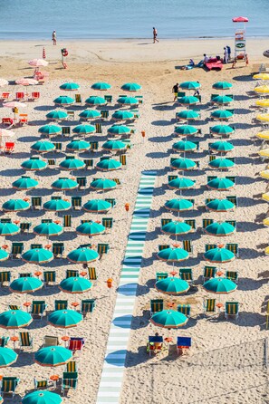 Una playa con hileras de sombrillas azules y verdes y sillas de playa a rayas.