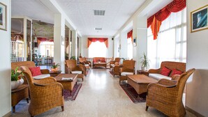 Un vestíbulo amplio con mobiliario de mimbre, un área de estar central y ventanas grandes con cortinas rojas.