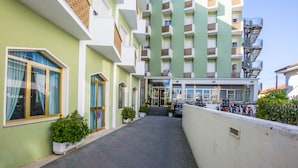 Un hotel de varios pisos con entrada central, zona de estar al aire libre y aparcamiento con bicicletas.
