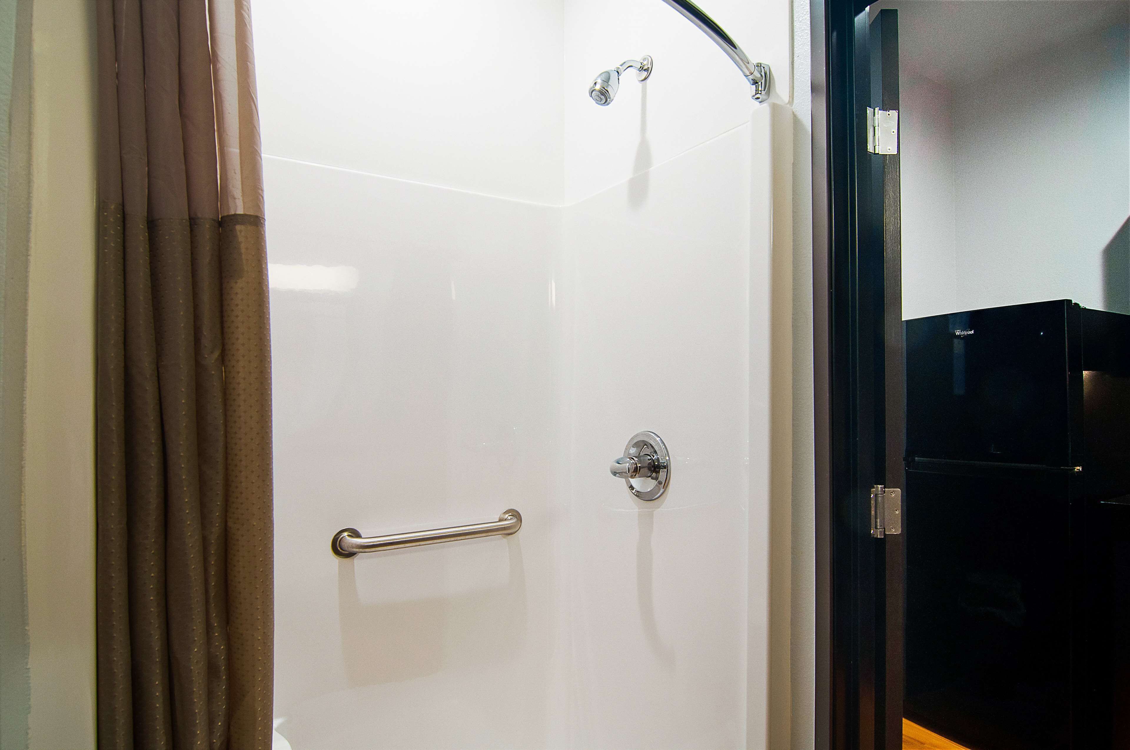Un baño con una puerta de ducha blanca, un pasamanos y un armario negro.