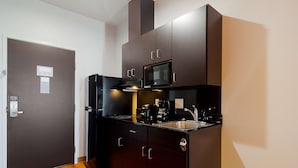 Une cuisine de taille réduite, dotée de meubles de rangement sombres, d’un four à micro-ondes et d’une machine à café.