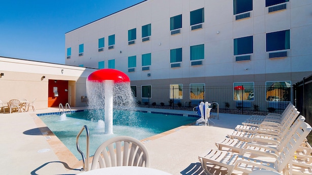 Une piscine avec une fontaine, des chaises longues et un bâtiment doté de nombreuses fenêtres en arrière-plan.