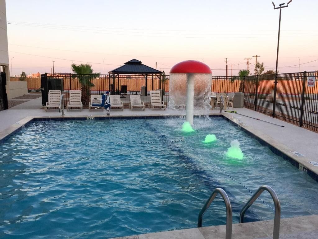 A swimming pool with a water fountain feature, surrounded by lounge chairs and a covered seating area.