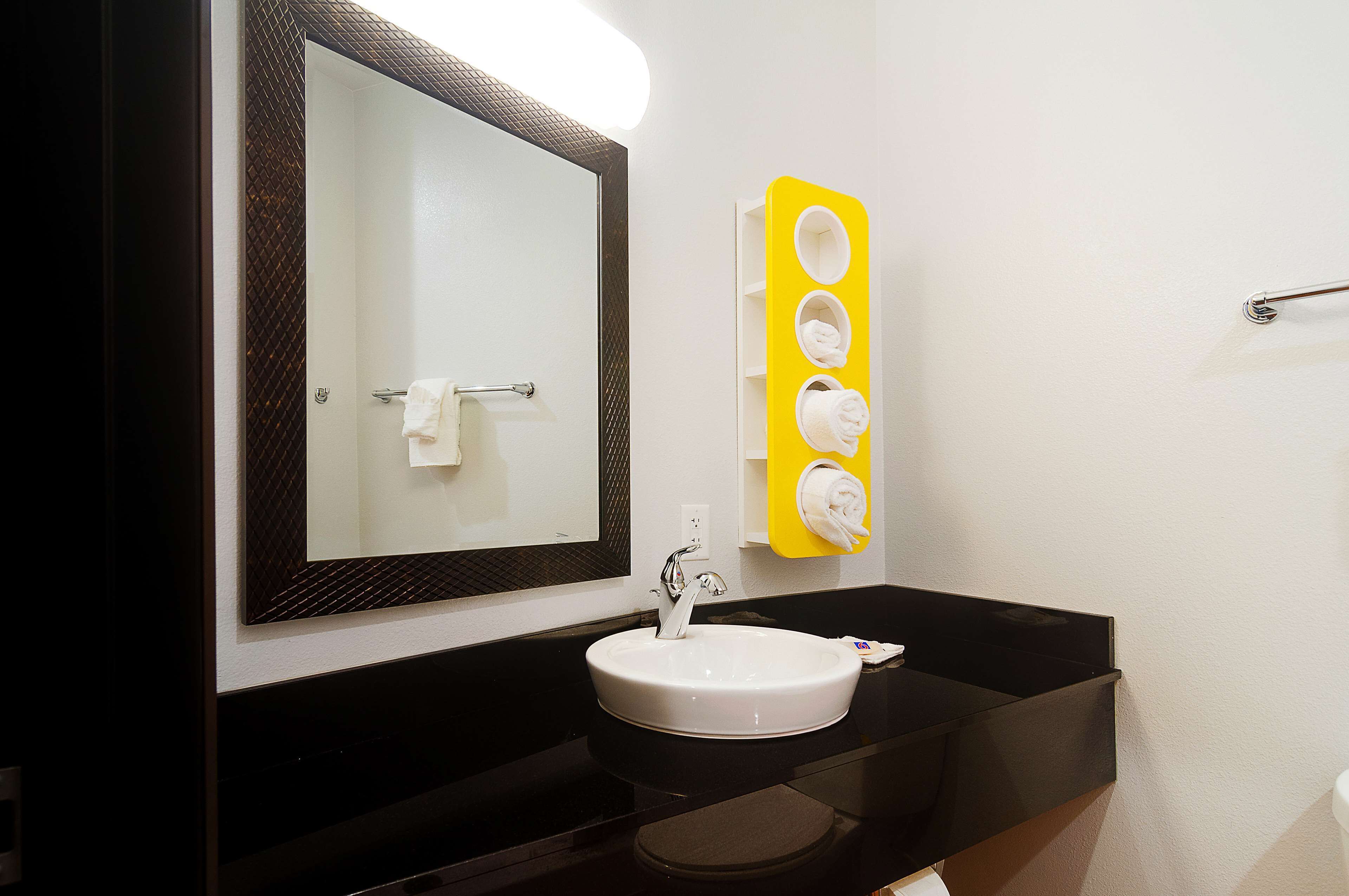 A bathroom with a white sink, a large mirror, and a yellow towel warmer.