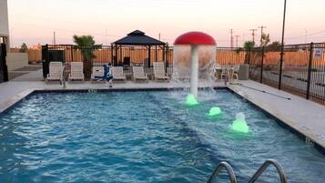 A swimming pool with a water fountain feature, surrounded by lounge chairs and a covered seating area.