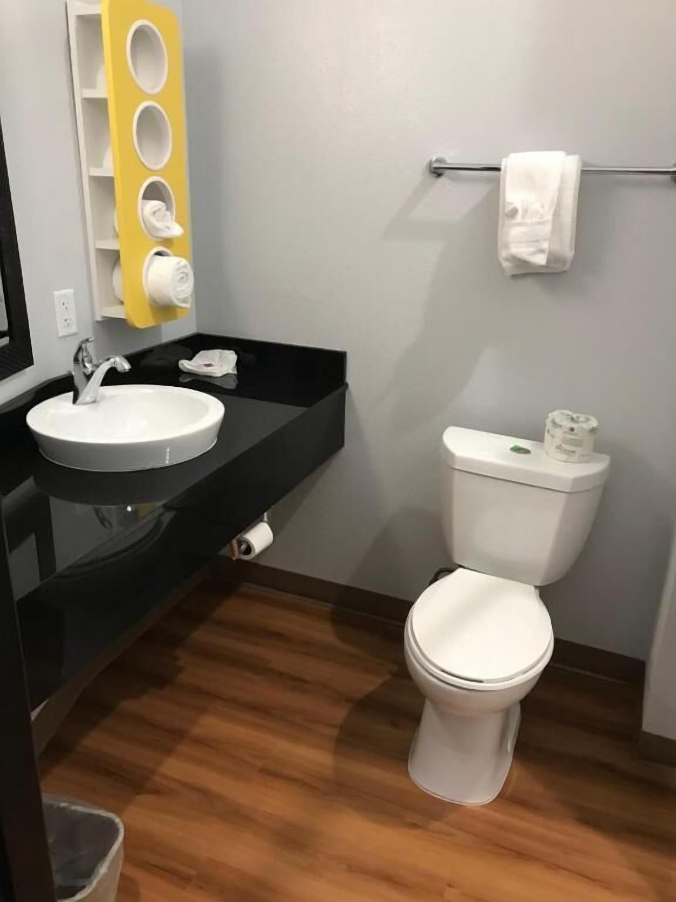 A bathroom with a white toilet, a black sink, and a yellow towel rack.