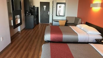 A hotel room with a bed, a desk, a chair, a kitchenette, and a mirror.