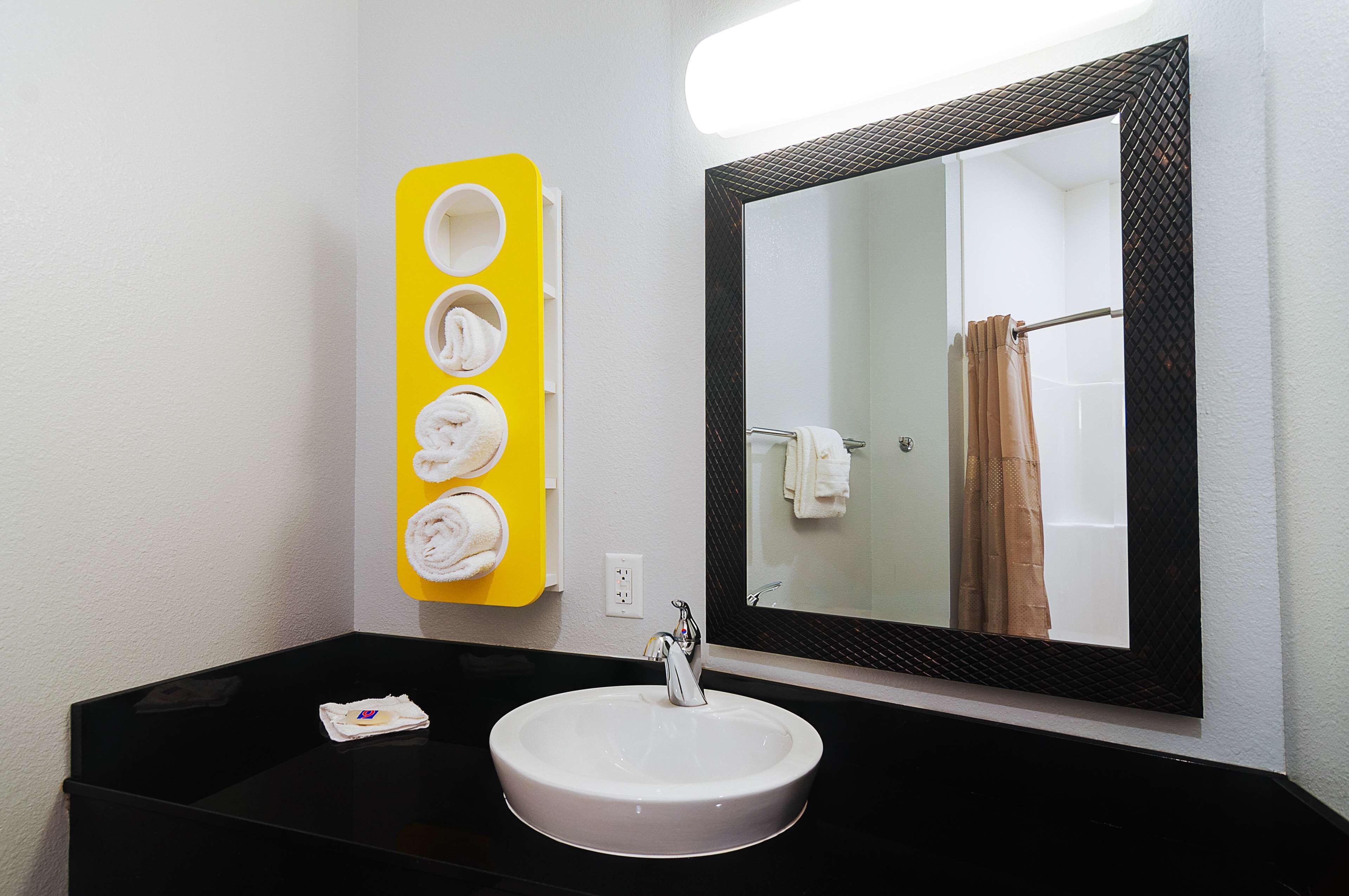 Un baño con un lavamanos blanco, un espejo con marco negro y un toallero amarillo con cuatro toallas.
