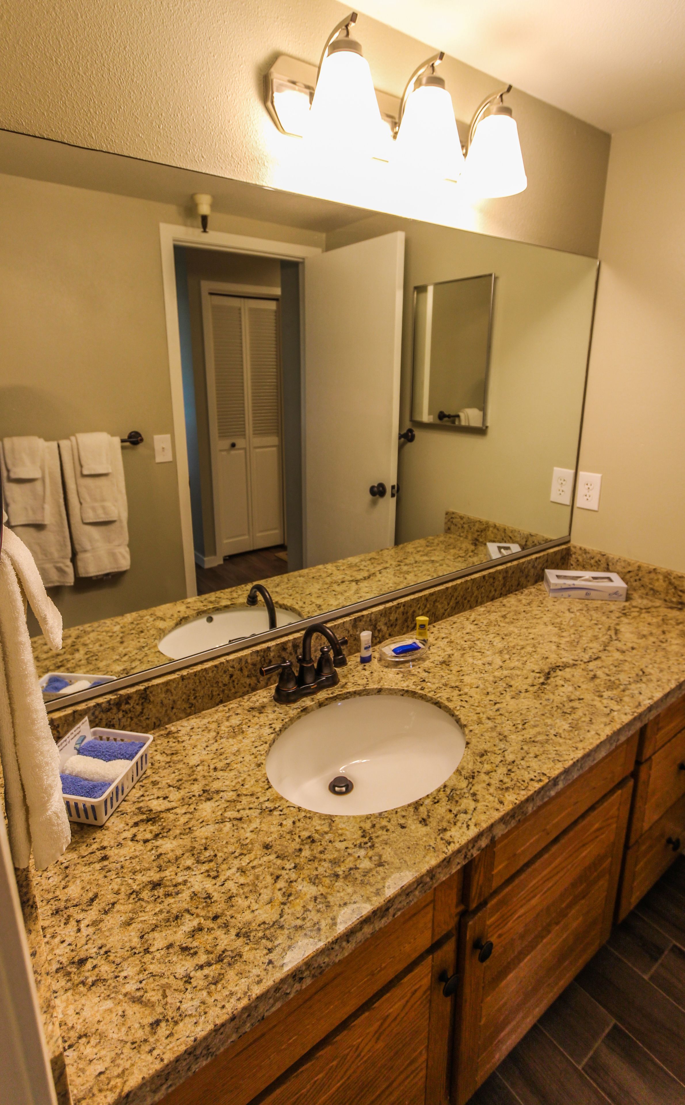 A bathroom with a granite countertop, two sinks, a mirror, and a towel rack.