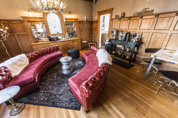A cozy living room with a curved red sofa, a coffee bar, and wooden paneling. - Ember Hostel (Denver)