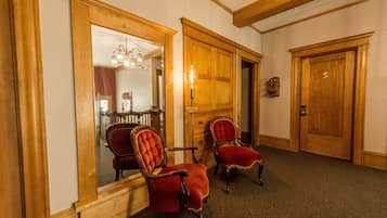 A room with two red upholstered chairs, wooden doors, and a mirror reflecting a dining area.