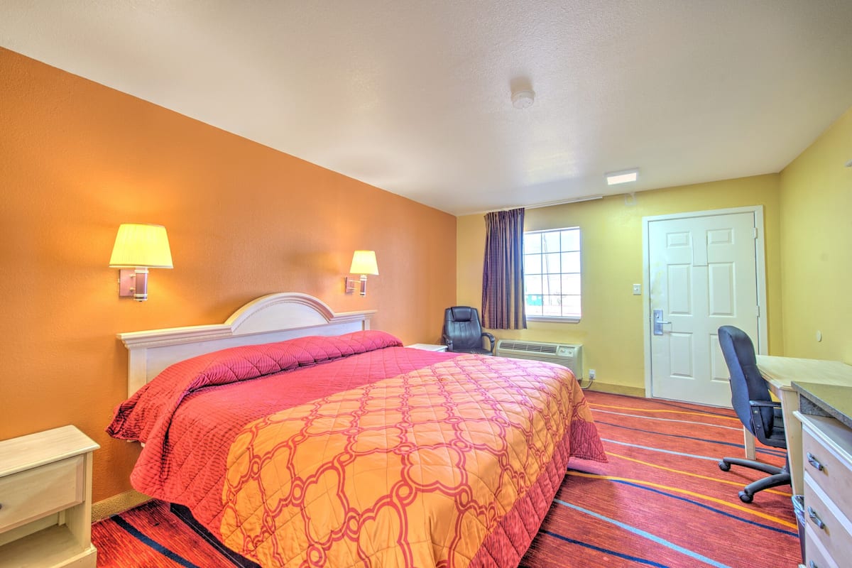 A hotel room with a large bed, two bedside lamps, a desk, a chair, and a door.
