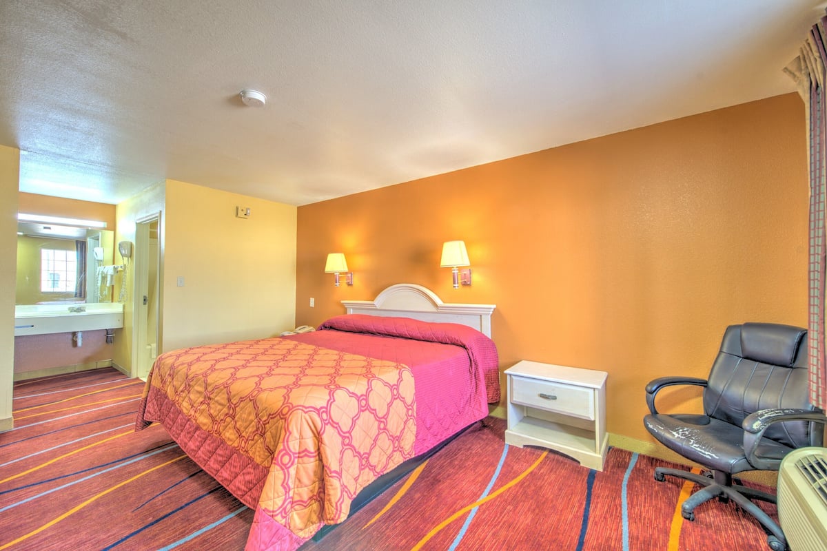 A hotel room with a bed, two bedside lamps, a chair, a nightstand, and a mirror.