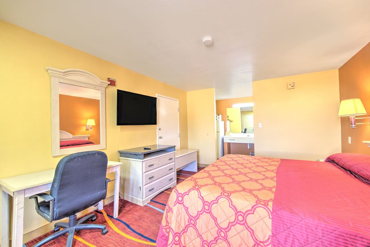 A hotel room with a bed, desk, chair, dresser, and a TV on the wall.