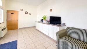 A living room with a sofa, a TV, a kitchen area, and a door.