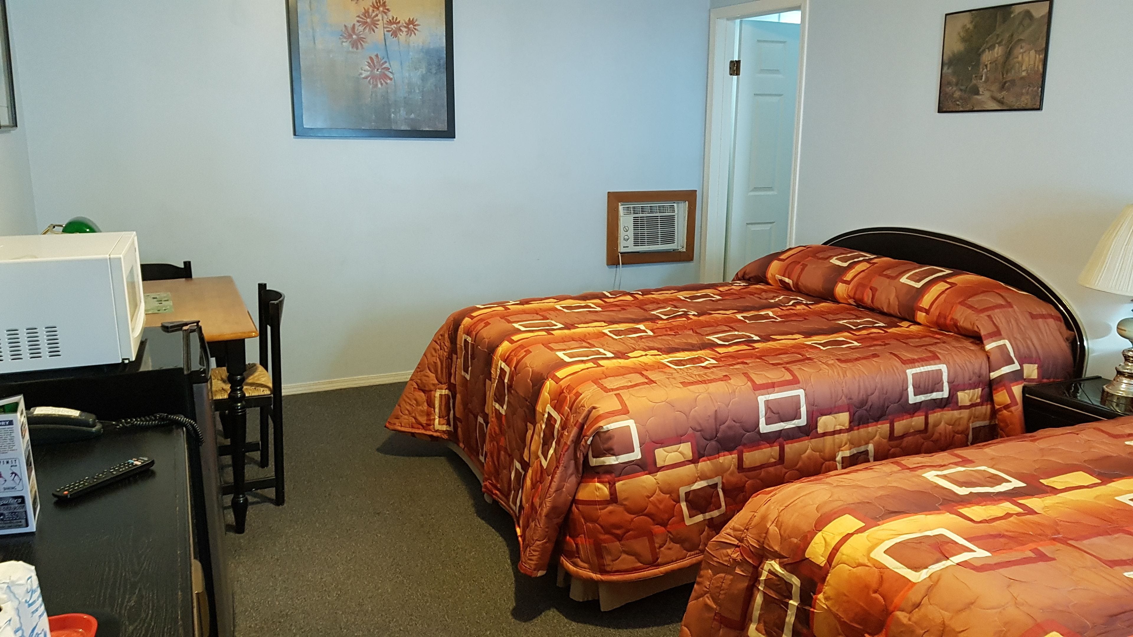 A hotel room with two beds, a desk, a chair, a microwave, and a door leading to another room.