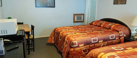 A hotel room with two beds, a desk, a chair, a microwave, and a door leading to another room.