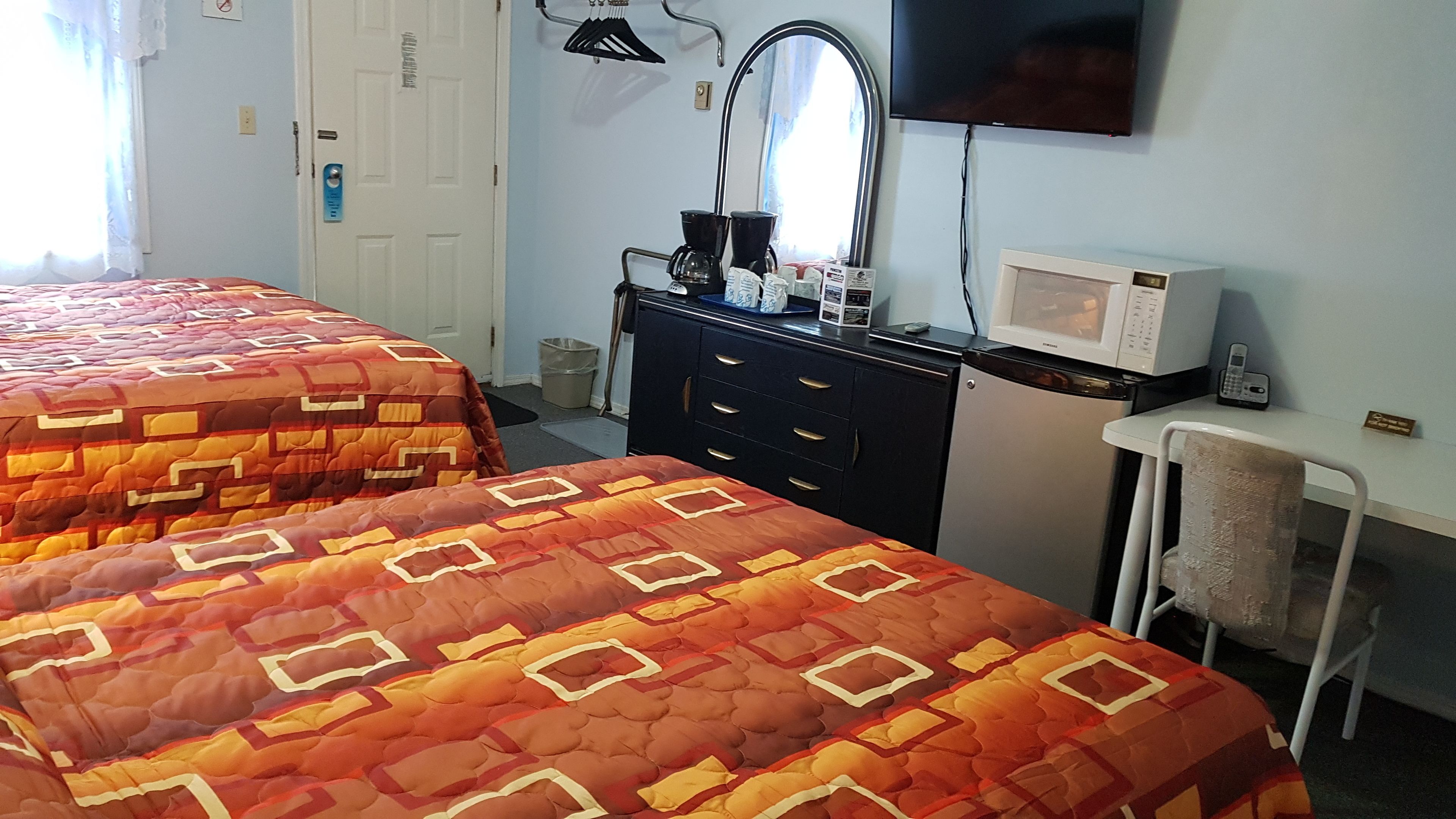 A hotel room with two beds, a dresser, a microwave, a chair, and a television.