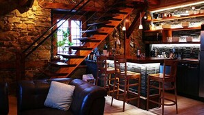 Un interior rústico con pared de piedra, escalera de madera, sofá de cuero y zona de bar con estantes.