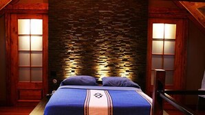 Un dormitorio con pared de piedra, una cama con ropa de cama azul y dos lámparas fijadas a la pared.