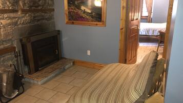 A room with a stone fireplace, a bed with striped bedding, and a painting of a coastal landscape.