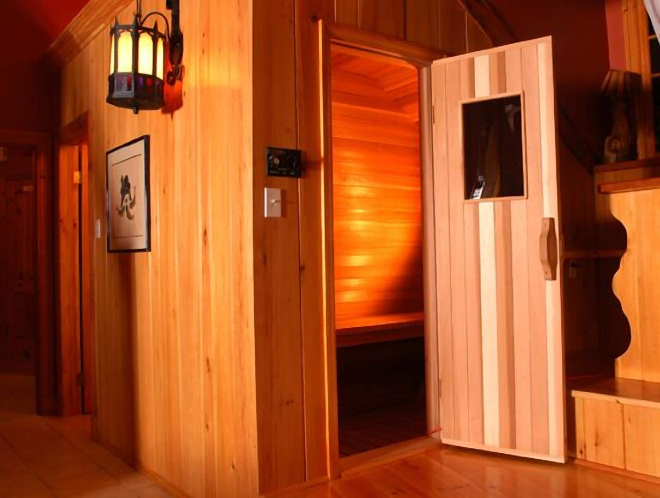 A wooden interior with a sauna room, a wooden door, and a wall-mounted light fixture.