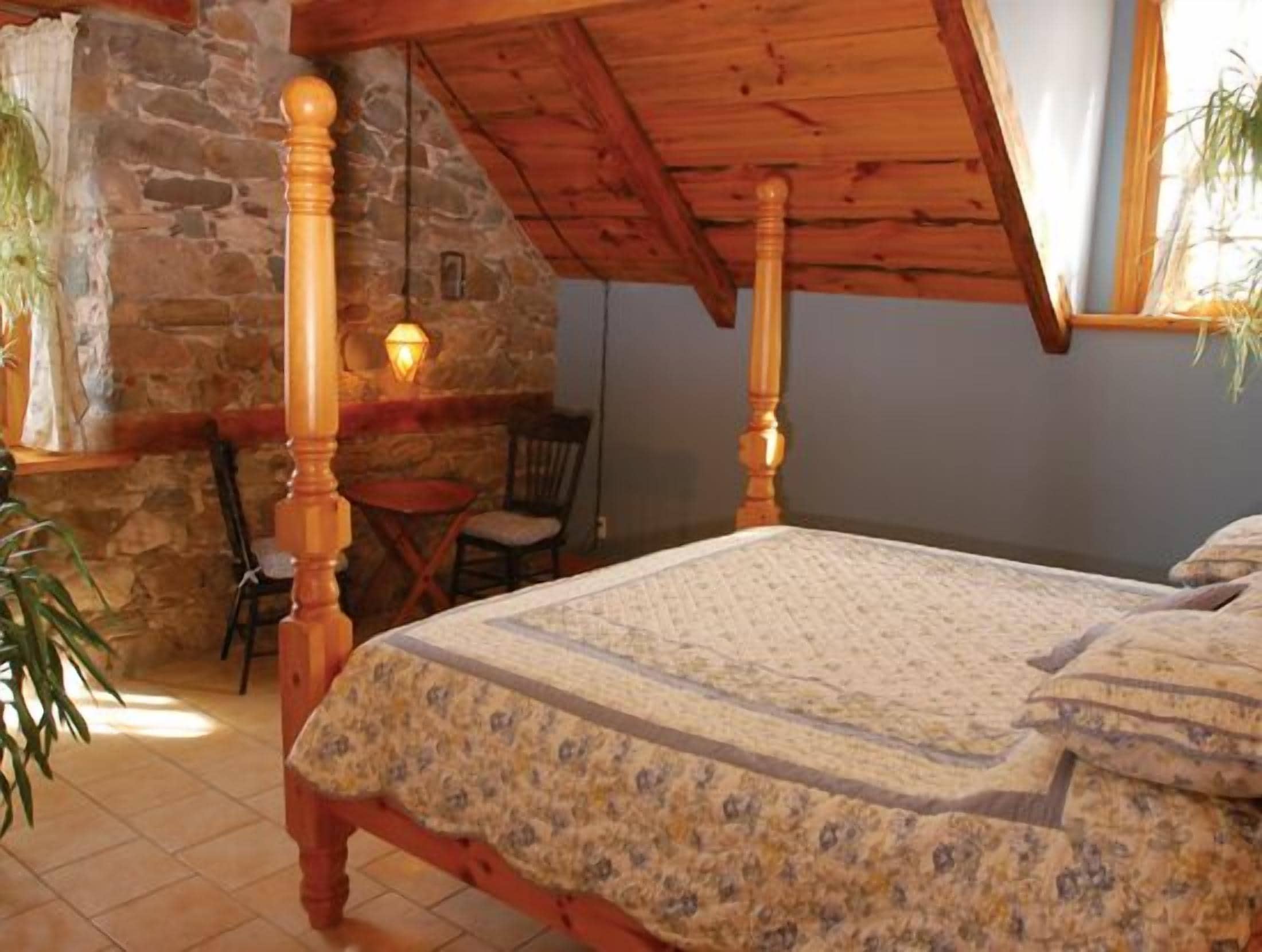 Un dormitorio con una cama de madera con dosel, una pared de piedra y una pequeña mesa con una silla.